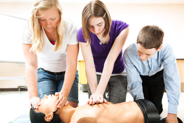 Students practicing CPR life saving techniques on a mannequin.