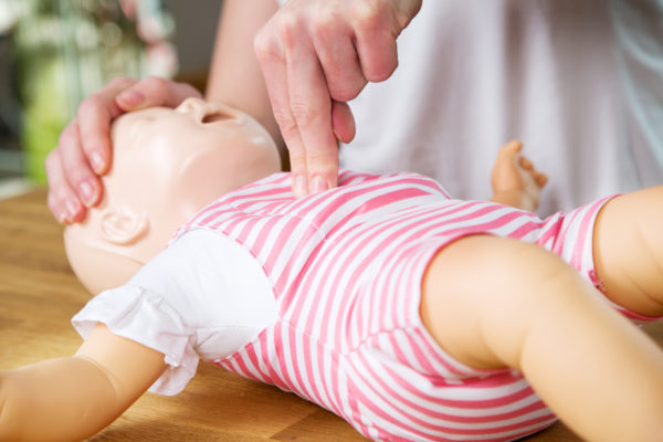 Woman showing infant CPR on training doll. Performing two finger chest compression.